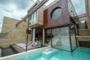 a woman sitting on a bench next to a house with a swimming pool at Fallingwater Pool Villa by Cross River Kwai in Kanchanaburi