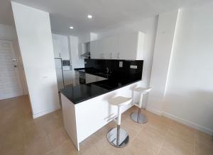 a white kitchen with a black counter and stools at Turquesa & Ambar Apartments Formentera in La Savina