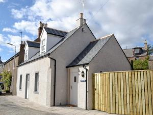 a white and gray house with a wooden fence at Keyland Cottage in Johnshaven