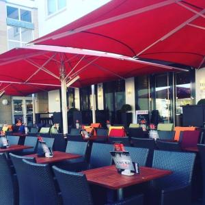 un restaurante con mesas y sillas con sombrillas rojas en Stadthotel Langenfeld en Langenfeld