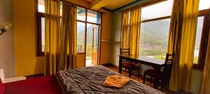 a bedroom with a bed and a desk and windows at La Vaca India Manali in Manāli