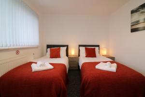 2 Betten in einem Zimmer mit roter Bettwäsche und weißen Handtüchern in der Unterkunft Signature - Atholl House Glasgow Airport in Paisley