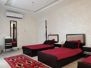 a bedroom with two beds with red sheets and a rug at The Legend Villa فيلا الاسطوره in Sowayma