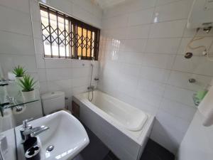 a white bathroom with a sink and a bath tub at NESTA BARRON -Home Away from Home in North Legon