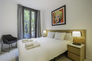 a bedroom with a white bed with a chair and a window at The White Flats Sant Antoni in Barcelona