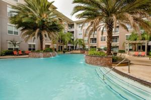 a large swimming pool with palm trees in front of a building at Resort-style Pool, Gym/Garage, 1Br, Medical Center in Houston