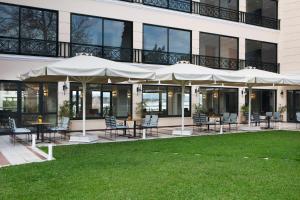 馬蒂的住宿－Ramada by Wyndham , Athens Club Attica Riviera，大楼前方的带桌椅和遮阳伞的天井。