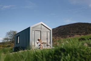 a man sitting in front of a green tiny house at Oaklane Glamping Cabins in Kenmare