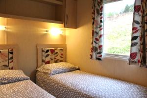 two beds in a small room with a window at Crannich Holiday Caravans in Killichronan