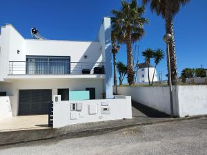 a white house with palm trees in front of it at Sunset Street Beach house in Lourinhã