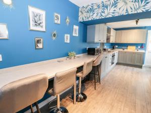 a kitchen with blue walls and a large counter with chairs at 23 Deganwy Avenue in Llandudno