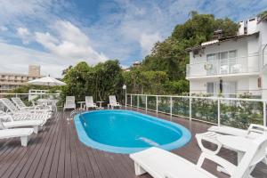ein Swimmingpool auf einer Terrasse mit weißen Stühlen und einem Gebäude in der Unterkunft Bombinhas Tourist Apart in Bombinhas