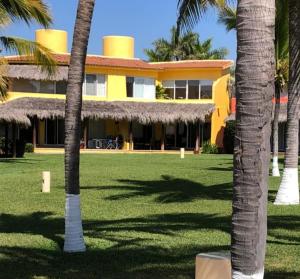 een geel gebouw met palmbomen ervoor bij Villas Playa Blanca in Zihuatanejo