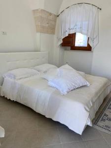 Cama blanca con sábanas blancas y ventana en Casa Nonna Renzina, en Locorotondo