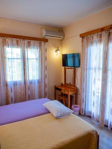 a bedroom with a bed and a television and windows at Eleni's Apartments & Studios 1 in Achílleion