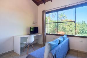 a living room with a blue couch and a desk and a window at Studios na Vermelhinha in Ubatuba