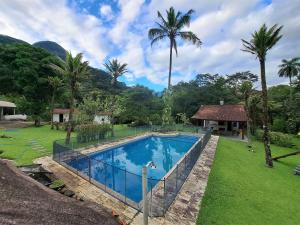 einen Pool in einem Garten mit Palmen in der Unterkunft Paradisíaco, piscina e churrasqueira em Guapi. in Guapimirim