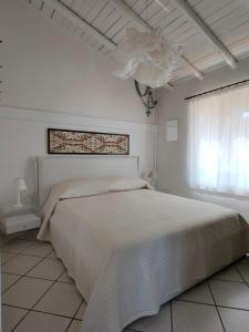 biała sypialnia z dużym łóżkiem i oknem w obiekcie Villa Unica - Appartamenti Alba e Tramonto w mieście Isola Rossa