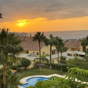 einen Sonnenuntergang über einem Resort mit Pool und Palmen in der Unterkunft Puerto Alto 6-3 with stunning sea-view in Estepona
