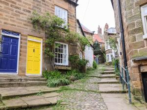 a cobblestone street in an old town with a yellow door at Delft Cottage in Robin Hood's Bay