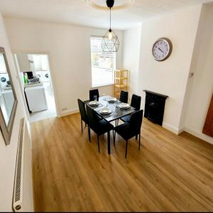 a dining room table with chairs and a clock on the wall at Comfortable 2 Bed House Near City Centre and M1 in Leicester