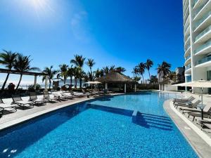 a swimming pool with lounge chairs and a building at Lujoso departamento frente al mar/camino al mar in Mazatlán