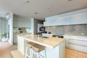 a kitchen with white cabinets and a kitchen island with stools at Marsden Suites Nautilus Orewa in Orewa