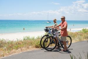 a man and woman standing next to a bike on the beach at Bayview Geographe Resort Busselton in Busselton