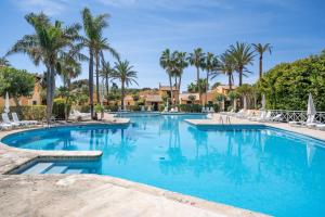 een groot zwembad met palmbomen in een resort bij Sensacions Menorca - Villas & Bungalows en complejo Pueblo Menorquín in Son Xoriguer