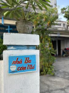 un cartel en una pared blanca con una planta. en nhà Ba cơm Má, en Phương Phi