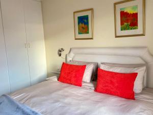 Una cama blanca con dos almohadas rojas. en Secure apartment, 500m from the beach Cathcart Road, Humewood en Summerstrand