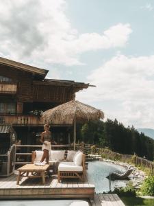 une femme assise sur un canapé sur une terrasse à côté d'une piscine dans l'établissement Jufenalm BOHO Hotel & Restaurant, à Maria Alm