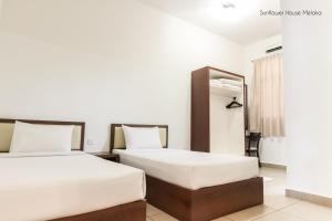 duas camas num quarto de hotel com paredes brancas em De Harmony Stay em Malaca