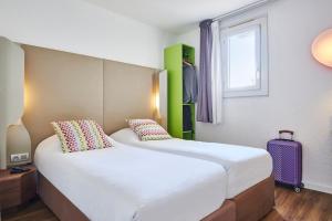 a bedroom with two beds and a window and a suitcase at Campanile Valence Nord - Bourg-Les-Valence in Bourg-lès-Valence