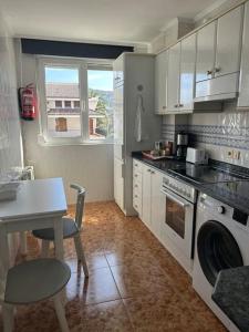 uma cozinha com armários brancos, uma mesa e uma cadeira em Playa de Berria - Precioso Apartamento con piscina, Garaje incluido e INTERNET em Santoña