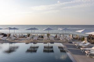 a swimming pool with chairs and umbrellas next to the ocean at Delta Hotels by Marriott Giardini Naxos in Giardini Naxos