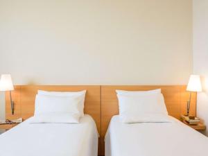 2 łóżka w pokoju hotelowym z białymi poduszkami w obiekcie Novotel Torino Corso Giulio Cesare w Turynie