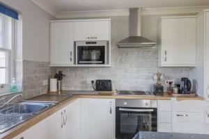 una cucina con armadi bianchi, lavandino e piano cottura di Bainvalley Cottages - The Shamba, sleeps 4 a Lincolnshire
