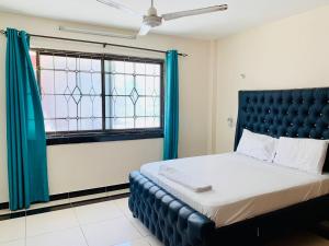 - une chambre avec un lit doté d'une tête de lit bleue et d'une fenêtre dans l'établissement Lux Suites Furaha Holiday Apartments Nyali, à Mombasa
