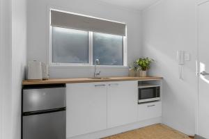 een witte keuken met een wastafel en een raam bij Marram Studio - Mangawhai Holiday Studio in Mangawhai
