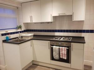 uma cozinha com armários brancos, um fogão e um lavatório em Bright 4-Bed house 15 min to Manchester Centre em Manchester
