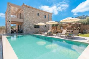 a swimming pool in front of a house with umbrellas at Claudio Stone House in Vasilikos