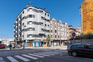 een groot wit gebouw in een stadsstraat met een auto bij MyHouseSpain - Acogedor piso nuevo en Gijón in Gijón