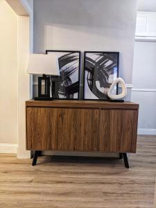 a wooden dresser with a lamp and pictures on it at Sweeney Stays, Cadzow Apartment in Hamilton