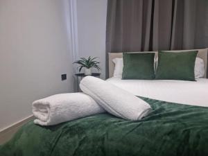 a bed with green and white pillows on it at Beautiful and Spacious 2-Bed Apartment: Home Away From Home in South Benfleet