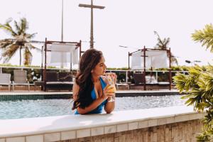 una mujer sentada junto a una piscina sosteniendo una bebida en Golden Tulip Natal Ponta Negra, en Natal