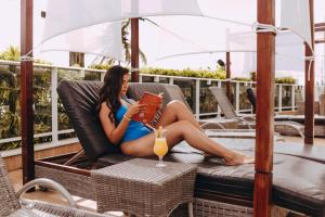 a woman sitting on a chair reading a book at Golden Tulip Natal Ponta Negra in Natal