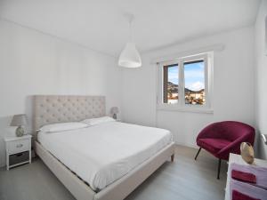 a white bedroom with a bed and a red chair at Caslano City Apartments in Caslano