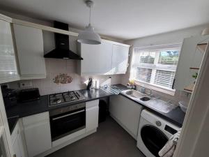 La cuisine est équipée de placards blancs et d'un four avec plaques de cuisson. dans l'établissement 2 Bedroom end of terrace house, à Wellington