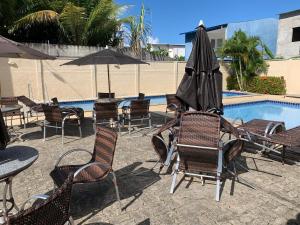 eine Gruppe Stühle und ein Sonnenschirm neben einem Pool in der Unterkunft Apartamento completo Ilheus in Ilhéus